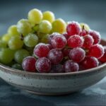 Tigela rústica com uvas vermelhas e verdes congeladas e cobertas de cristais de gelo, uma dica refrescante de como aproveitar uvas murchas.